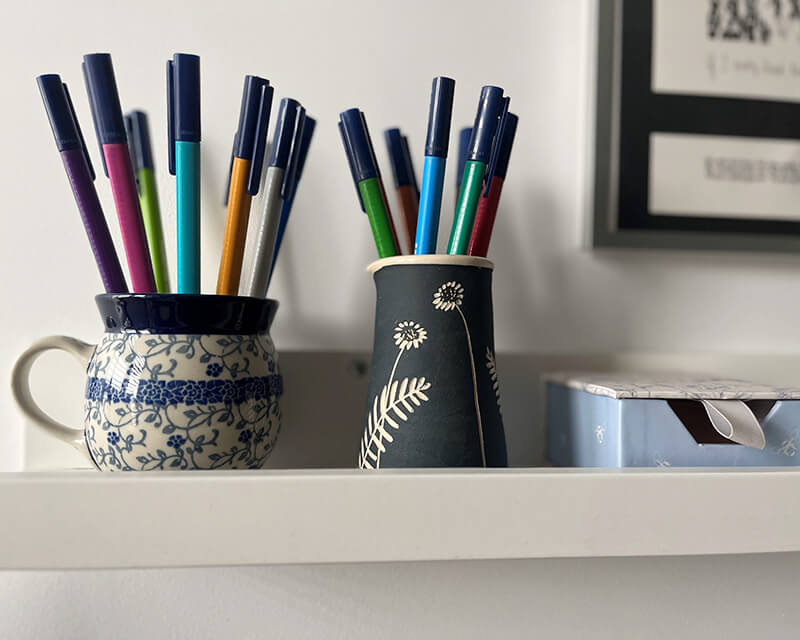 Colourful pens in cups, sitting on a shelf